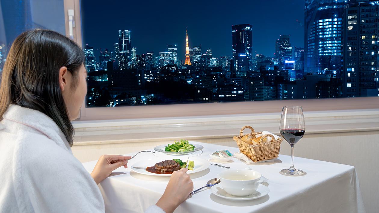 ザ・プリンス さくらタワー東京の「インルームダイニング」で、お部屋から夜景を眺めながらディナーを愉しむ女性客。